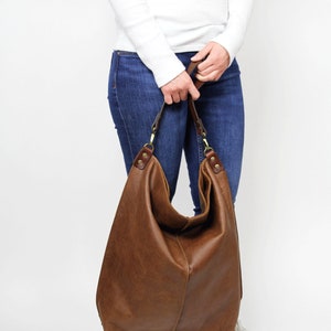 Puede incluir: Un bolso tote de cuero marr&oacute;n con una correa larga. El bolso es grande y espacioso, y tiene un estilo informal y relajado.