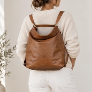 Peut inclure: Un sac à dos marron moyen, souple et à la finition lisse, doté d'une large ouverture supérieure, d'une poignée supérieure unique et de deux bretelles réglables fixées au panneau arrière, offrant un compartiment principal spacieux.