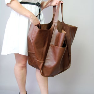 May include: A large brown leather tote bag with a wide opening and two long handles. The bag is made of soft, supple leather and has a casual, relaxed look.
