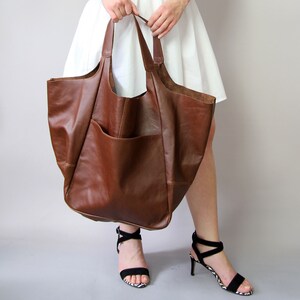 May include: A large brown leather tote bag with a single pocket on the front. The bag has two long straps.