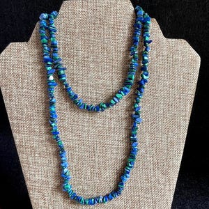 May include: A long necklace composed of numerous small, irregular, tumbled stone chips in vibrant shades of royal blue and deep forest green. The stones are strung together in a continuous strand, creating a textured, multi-layered appearance.