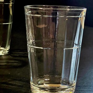 May include: Two clear, rectangular-shaped drinking glasses. The glasses are empty and sit on a dark surface. The glasses have a classic, simple design, perfect for water, juice, or other beverages.