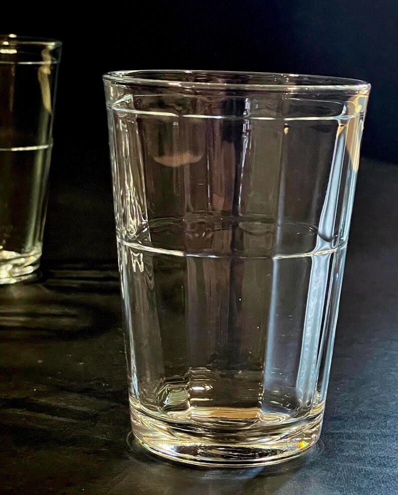May include: Two clear, rectangular-shaped drinking glasses. The glasses are empty and sit on a dark surface. The glasses have a classic, simple design, perfect for water, juice, or other beverages.