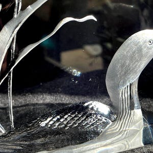 May include: A clear glass sculpture featuring a swan with etched details. The swan's body has a textured pattern, and the neck and head are smooth. The sculpture is set against a dark background, highlighting the intricate design.