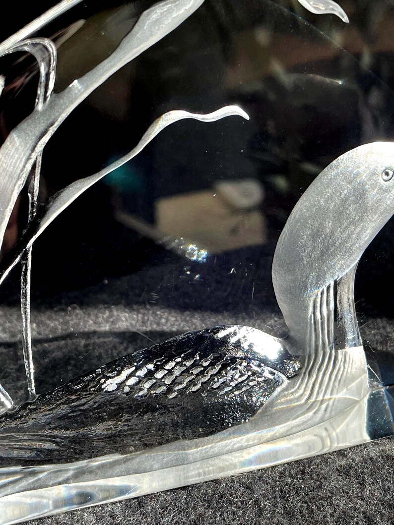 May include: A clear glass sculpture featuring a swan with etched details. The swan's body has a textured pattern, and the neck and head are smooth. The sculpture is set against a dark background, highlighting the intricate design.