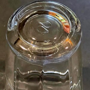 May include: Clear glass tumbler with a thick, rounded base. The bottom of the glass features a stylized design and the number "42". The glass has a faceted design on the sides.