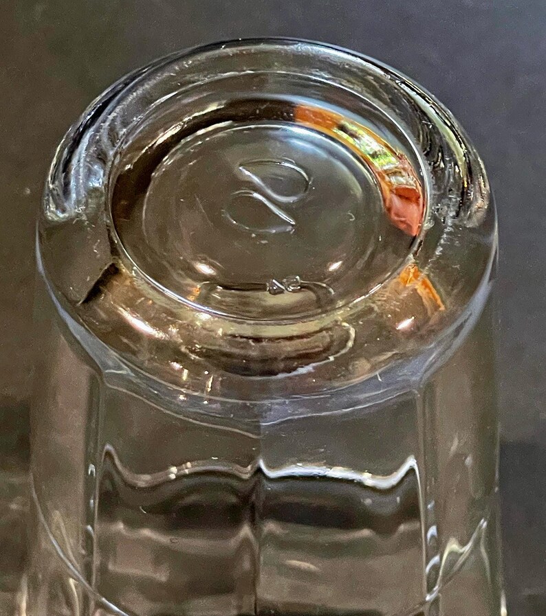 May include: Clear glass tumbler with a thick, rounded base. The bottom of the glass features a stylized design and the number "42". The glass has a faceted design on the sides.