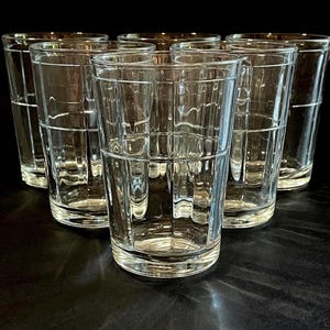 May include: Six clear, textured drinking glasses arranged in a group. The glasses have a rectangular grid pattern and a simple, elegant design. The glasses are empty and appear to be made of glass.