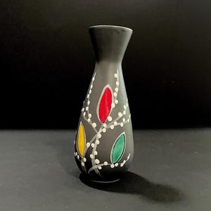 May include: A black ceramic vase with a white floral design and colorful accents. The vase has a narrow neck and a rounded body.