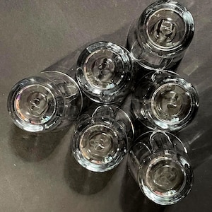 May include: Six clear, stemmed drinking glasses arranged in a circular pattern. The glasses are made of transparent glass, with a detailed base design. The image is taken from a top-down perspective, showcasing the glasses' bottoms.