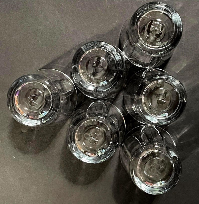 May include: Six clear, stemmed drinking glasses arranged in a circular pattern. The glasses are made of transparent glass, with a detailed base design. The image is taken from a top-down perspective, showcasing the glasses' bottoms.