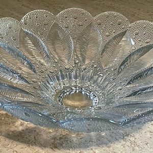May include: A clear glass bowl with a scalloped edge and a textured design of leaves and dots. The bowl is perfect for serving fruit, snacks, or other treats.