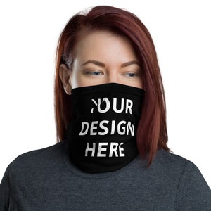 May include: Black neck gaiter with the text "YOUR DESIGN HERE" in white. The neck gaiter is worn around the neck and covers the lower face. The person in the image is wearing a dark gray shirt.