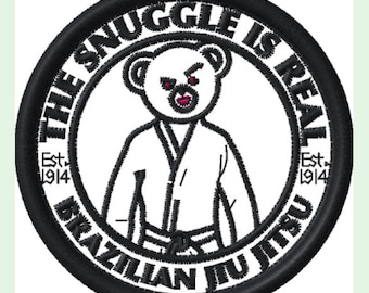 May include: Black and white embroidered patch with a white bear wearing a white gi and a black belt. The text around the bear reads "The Snuggle Is Real" with "Est. 1914" on either side. The bottom of the patch reads "Brazilian Jiu Jitsu".