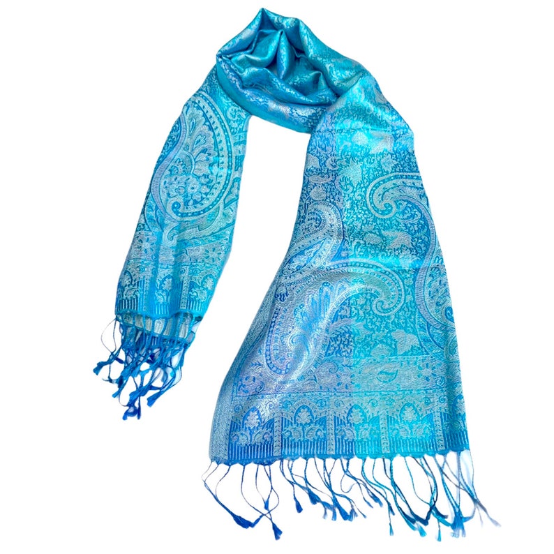 May include: A blue paisley patterned scarf with fringed edges. The scarf is made of a soft, silky material.
