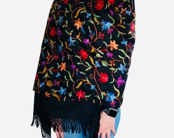 May include: A black shawl with colorful floral embroidery. The shawl has a fringe border and is draped over a person's shoulders.