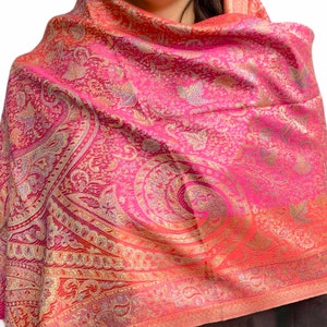 May include: A pink and gold paisley patterned scarf with a gradient effect. The scarf is made of a soft, luxurious fabric and is perfect for adding a touch of elegance to any outfit.