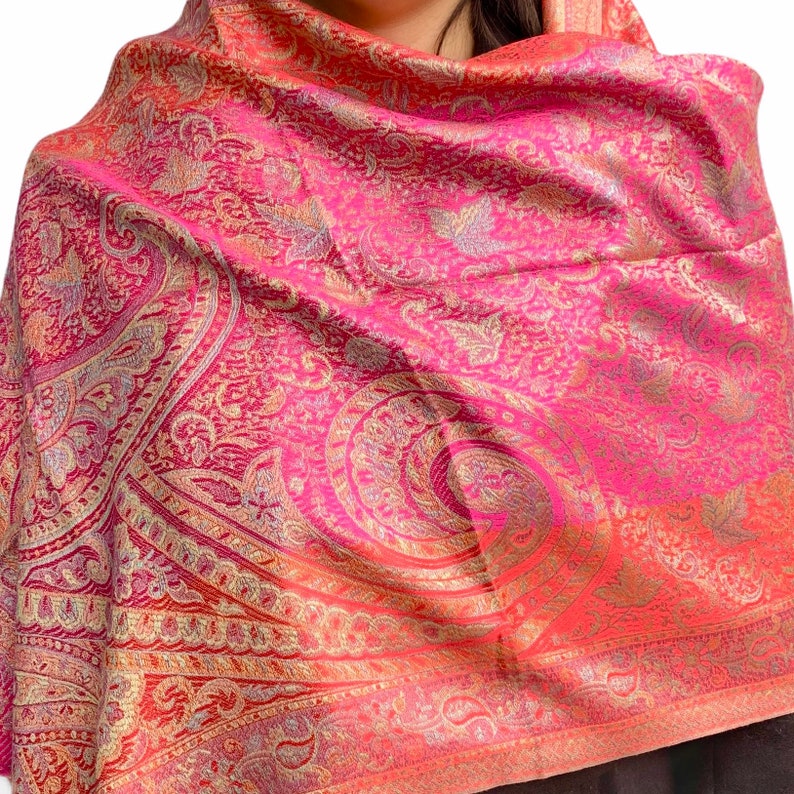 May include: A pink and gold paisley patterned scarf with a gradient effect. The scarf is made of a soft, luxurious fabric and is perfect for adding a touch of elegance to any outfit.