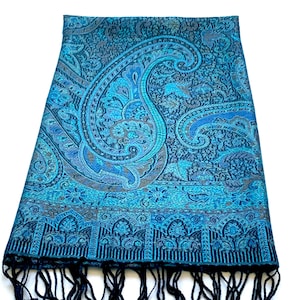 May include: A blue paisley patterned scarf with black fringe. The scarf has a detailed design with a variety of shades of blue and black.