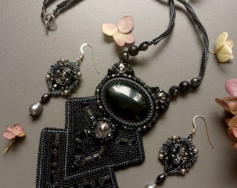 May include: A black beaded necklace with a large black stone pendant and matching earrings. The pendant is made of two square shapes with a smaller square in the centre. The earrings are a smaller version of the pendant.