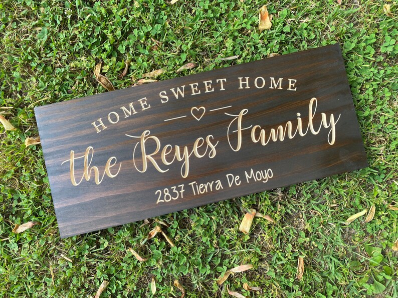 May include: A dark brown wooden sign with the text "Home Sweet Home" and a small heart symbol. Below the text is the name "the Reyes Family" and the address "2837 Tierra De Moyo".