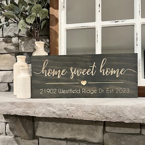 以下が含まれることがあります： 「home sweet home」という金色の文字が書かれた濃い茶色の木製看板。看板には小さな金色のハートと「21902 Westfield Ridge Dr. Est 2023」という金色の文字も書かれている。