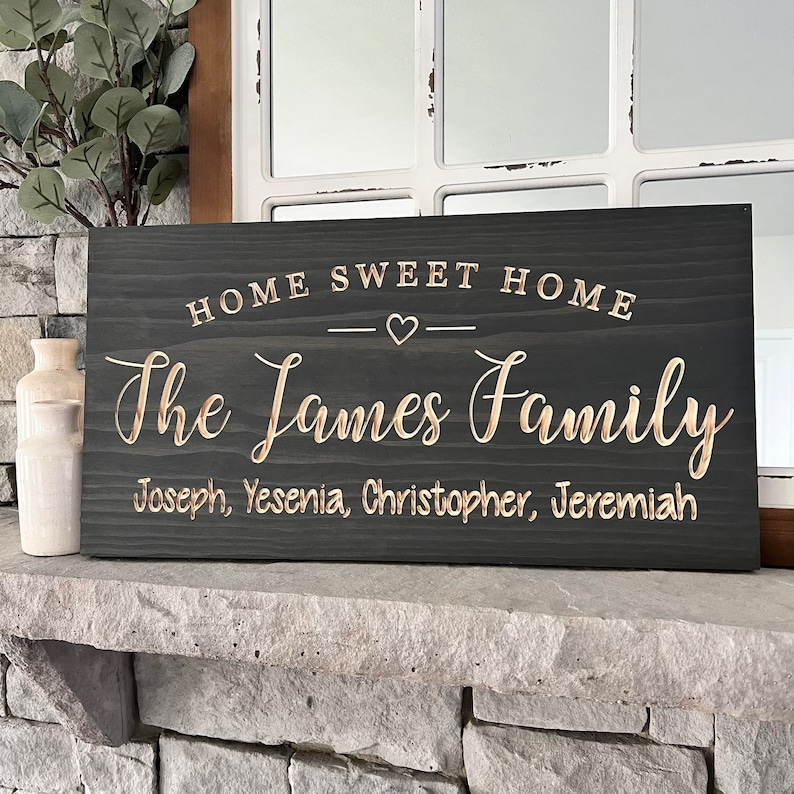 May include: A dark gray wooden sign with the text "Home Sweet Home" and a heart symbol. Below the text is "The James Family" with the names Joseph, Yesenia, Christopher, and Jeremiah.