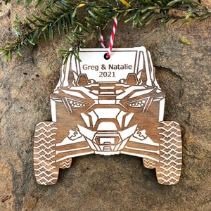 May include: A white wooden ornament shaped like a side-by-side off-road vehicle with the text "Greg & Natalie 2021" on the top.