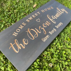 May include: A black wooden sign with the text "Home Sweet Home the Dixon Family Glenn Sheryl Snoopy" in gold lettering. A heart symbol is between "Home" and "the".