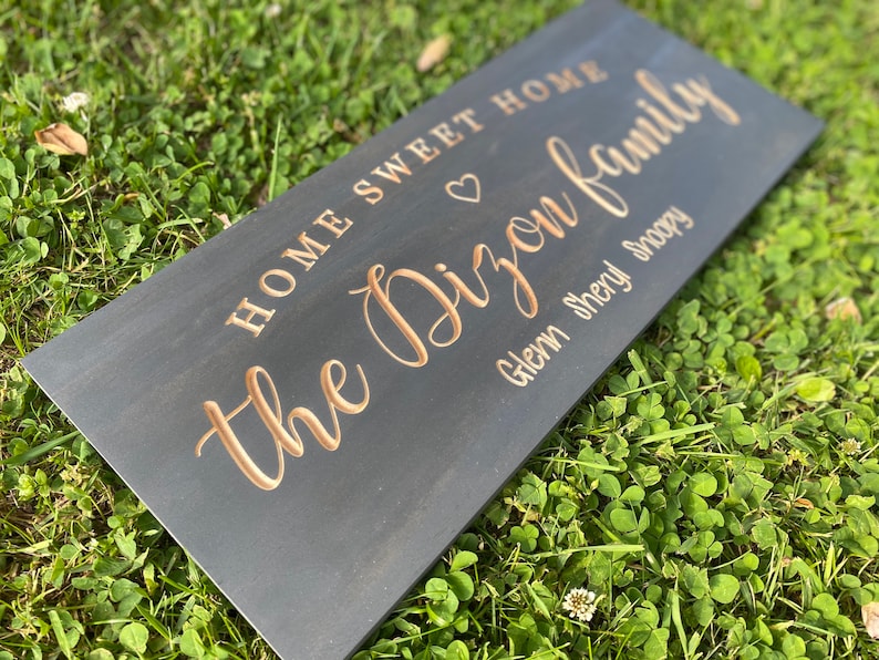 May include: A black wooden sign with the text "Home Sweet Home the Dixon Family Glenn Sheryl Snoopy" in gold lettering. A heart symbol is between "Home" and "the".