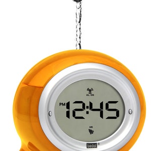 May include: Orange waterproof digital clock with a silver trim and a white display showing the time 12:45 PM. The clock is being sprayed with water from a tap.