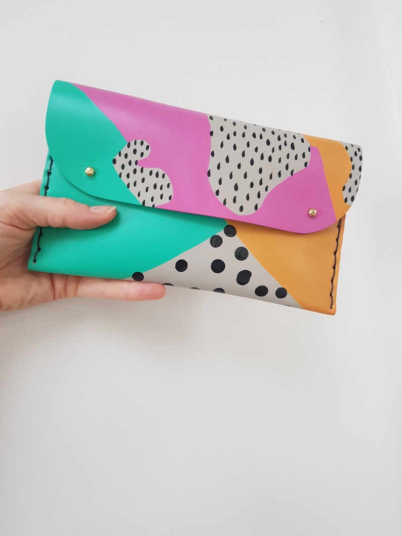 May include: A colorful leather clutch with a geometric pattern in shades of pink, green, yellow, and black. The clutch has a flap closure and gold-toned hardware.