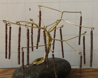 May include: A wire tree sculpture with brown beads hanging from the branches. The tree is standing on a dark grey rock.