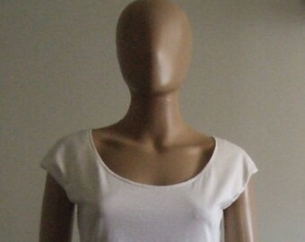 May include: A white scoop-neck top with short sleeves. The top is made of a soft, light-colored fabric and has a simple, classic design. The top is displayed on a mannequin. The mannequin is wearing black pants.