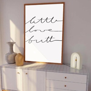 Peut inclure: Une impression encadrée avec le texte "little love but" écrit en cursive noire sur un fond blanc.