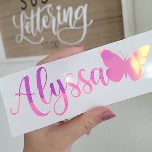 May include: A white vinyl decal with the name "Alyssa" written in pink and purple script with a holographic pink butterfly to the right.