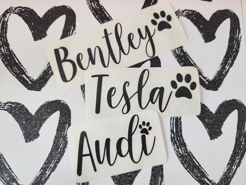 May include: Three white labels with black paw prints and names written in black cursive. The names are Bentley, Tesla, and Audi.
