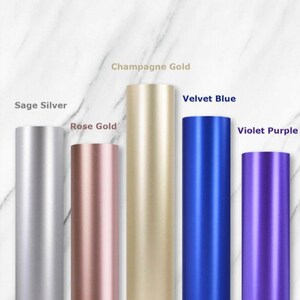 May include: Five different colored vinyl rolls, from left to right: Sage Silver, Rose Gold, Champagne Gold, Velvet Blue, and Violet Purple.