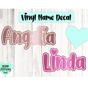 May include: Vinyl name decals in shades of pink and brown, with the names "Angelina" and "Linda" displayed. A light blue heart shape and the text "Vinyl Name Decal" are also present. The image includes a logo for "Susan Lettering Studio".