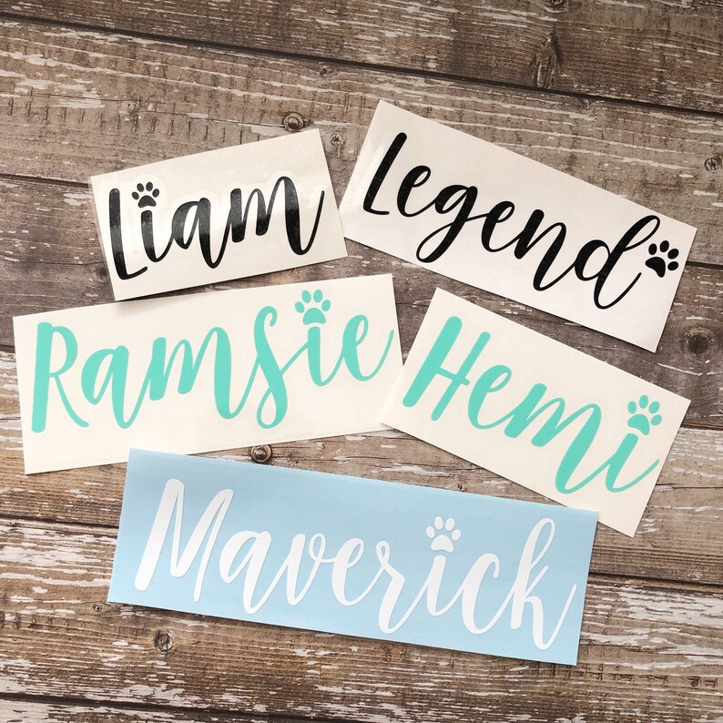 May include: Five personalized pet name decals with paw prints. The names are Liam, Legend, Ramsie, Hemi, and Maverick. The decals are on a wood background.