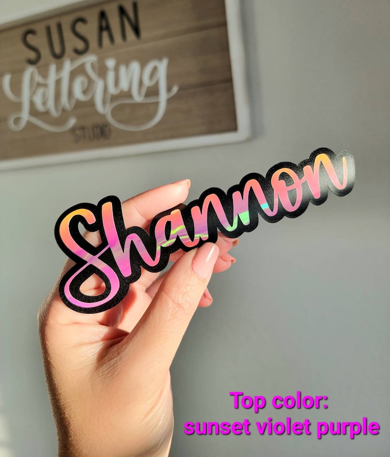 May include: A black vinyl sticker with the name "Shannon" written in a cursive font. The sticker has a holographic finish with a sunset violet purple top color.