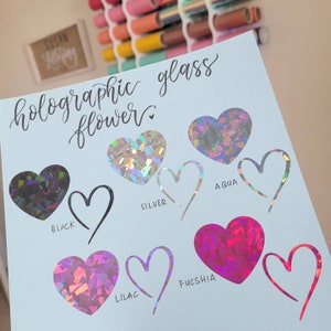 May include: A blue card with the text "holographic glass flower" written in black cursive. The card shows different colors of holographic vinyl in heart shapes. The colors are black, silver, aqua, lilac, and fuchsia.