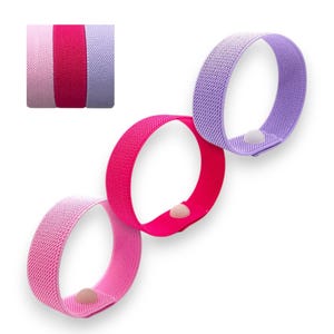 Könnte beinhalten: Drei farbige elastische Bänder in Rosa, Fuchsia und Lavendel, jedes mit einem kleinen, runden Verschluss. Ein kleineres Bild zeigt die Bänder gestapelt. Diese Bänder sind für verschiedene Zwecke konzipiert.