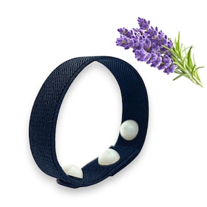 May include: A black fabric wristband with three white acupressure beads. The wristband is designed to help relieve nausea and motion sickness.