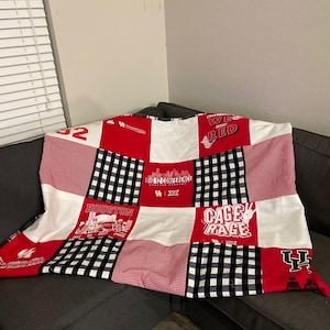 May include: A patchwork quilt in red, white, and black. The quilt features squares of gingham, solid colours, and text graphics. The text includes "HOUSTON", "CAGE RAGE", and "BIG 12 CONFERENCE".