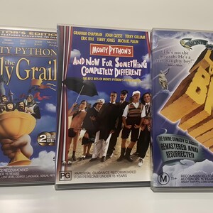Może przedstawiać: Trzy zestawy DVD Monty Pythona. Tytuły obejmują "Monty Python and the Holy Grail", "And Now For Something Completely Different" i "Żywot Briana". Okładki zawierają zdjęcia obsady i tytuły film&oacute;w pogrubioną czcionką. Płyty DVD są w przezroczystych plastikowych etui.