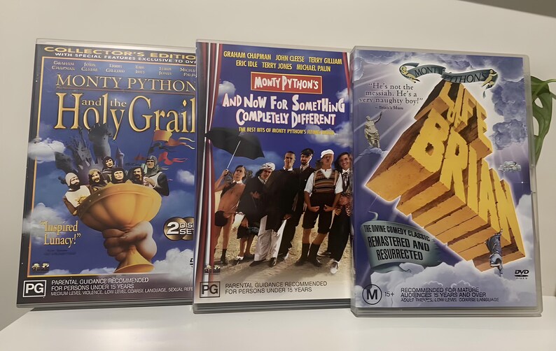 Może przedstawiać: Trzy zestawy DVD Monty Pythona. Tytuły obejmują "Monty Python and the Holy Grail", "And Now For Something Completely Different" i "Żywot Briana". Okładki zawierają zdjęcia obsady i tytuły film&oacute;w pogrubioną czcionką. Płyty DVD są w przezroczystych plastikowych etui.