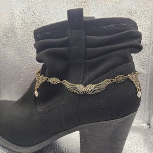 May include: A pair of black ankle boots with a gold and crystal ankle boot charm featuring a pair of wings.