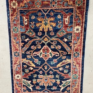 Puede incluir: Una alfombra azul y roja con un diseño persa tradicional. La alfombra tiene un medallón central con motivos florales y un borde con patrones geométricos.