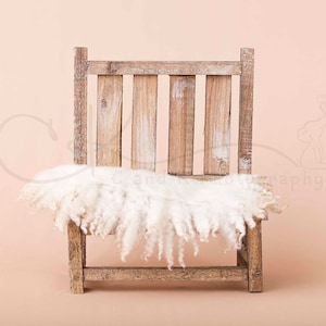 Puede incluir: Una silla de madera rústica con una manta de piel de oveja blanca y esponjosa drapeada sobre el asiento. La silla está colocada sobre un fondo de color melocotón claro.